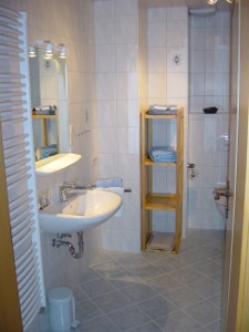 Blick ins Badezimmer, ein Handtuchheizkörper, das Waschbecken und ein Regal sind sichtbar.